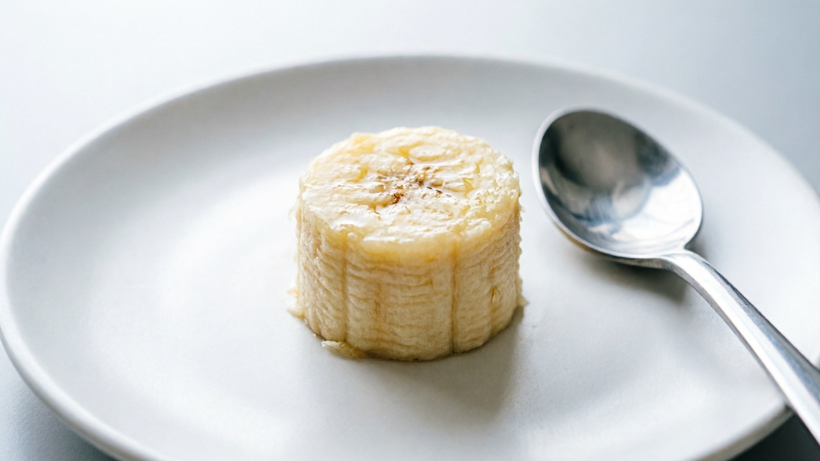 Thumbnail-sized piece of banana on a clean plate, with a teaspoon for scale comparison