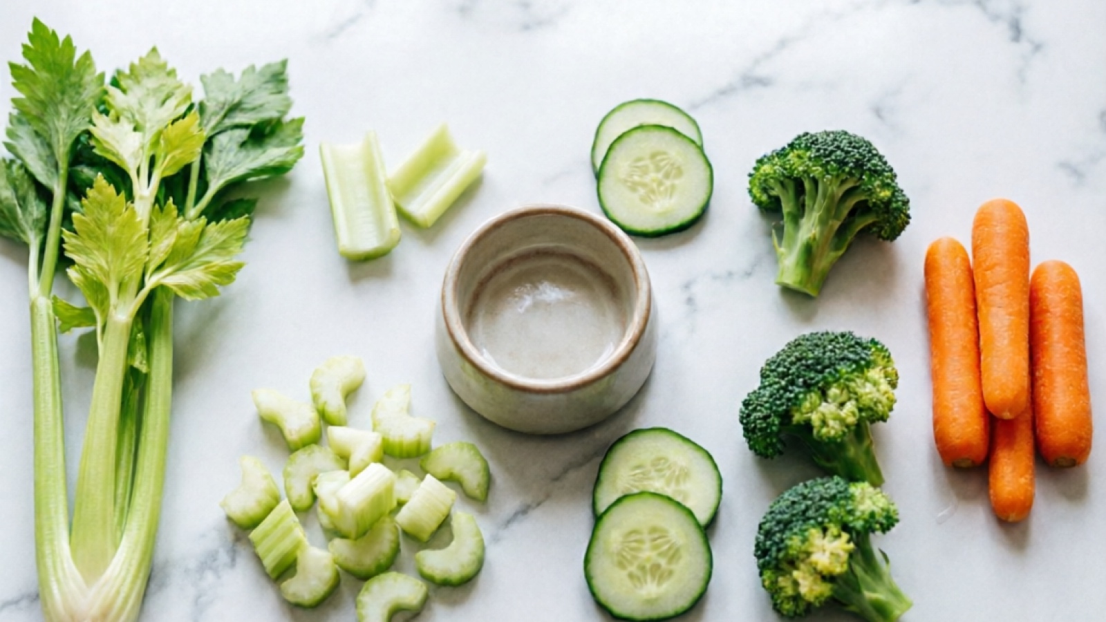 Comparison of celery leaves, celery stalk pieces, cucumber slices, broccoli florets, and baby carrot sticks arranged for hamster feeding