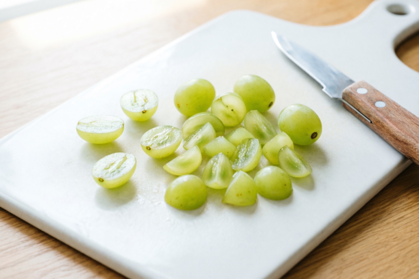 Seedless grape halved to confirm no seeds before feeding Halved seedless green grape showing no seeds inside, next to a small knife on a clean cutting board